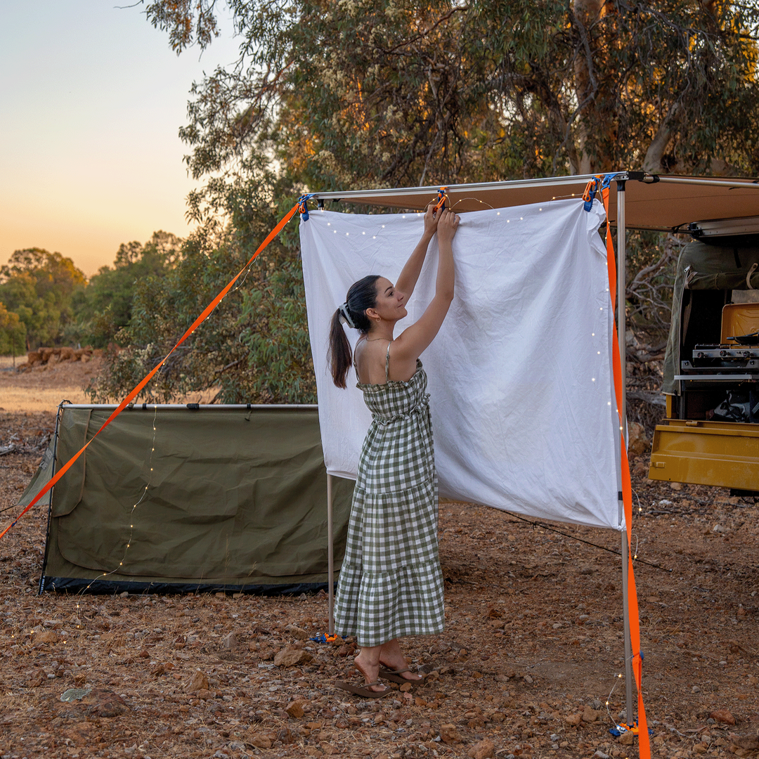 Woman setting up a camping setup with a tent and canopy in a natural outdoor setting.